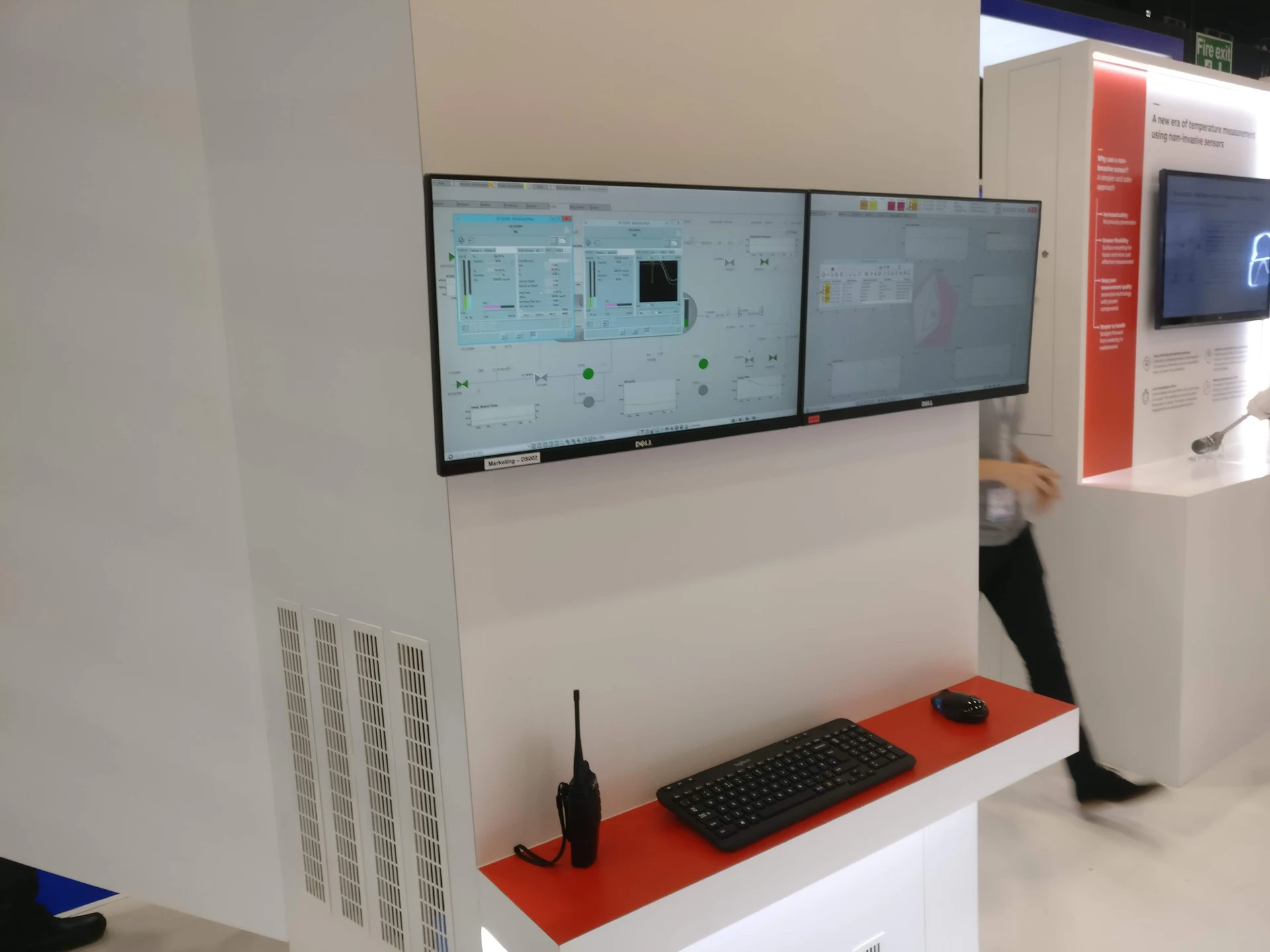 Two monitors at the ABB exhibition stand showing the System 800xA process interface and instrument faceplates above a keyboard and mouse.