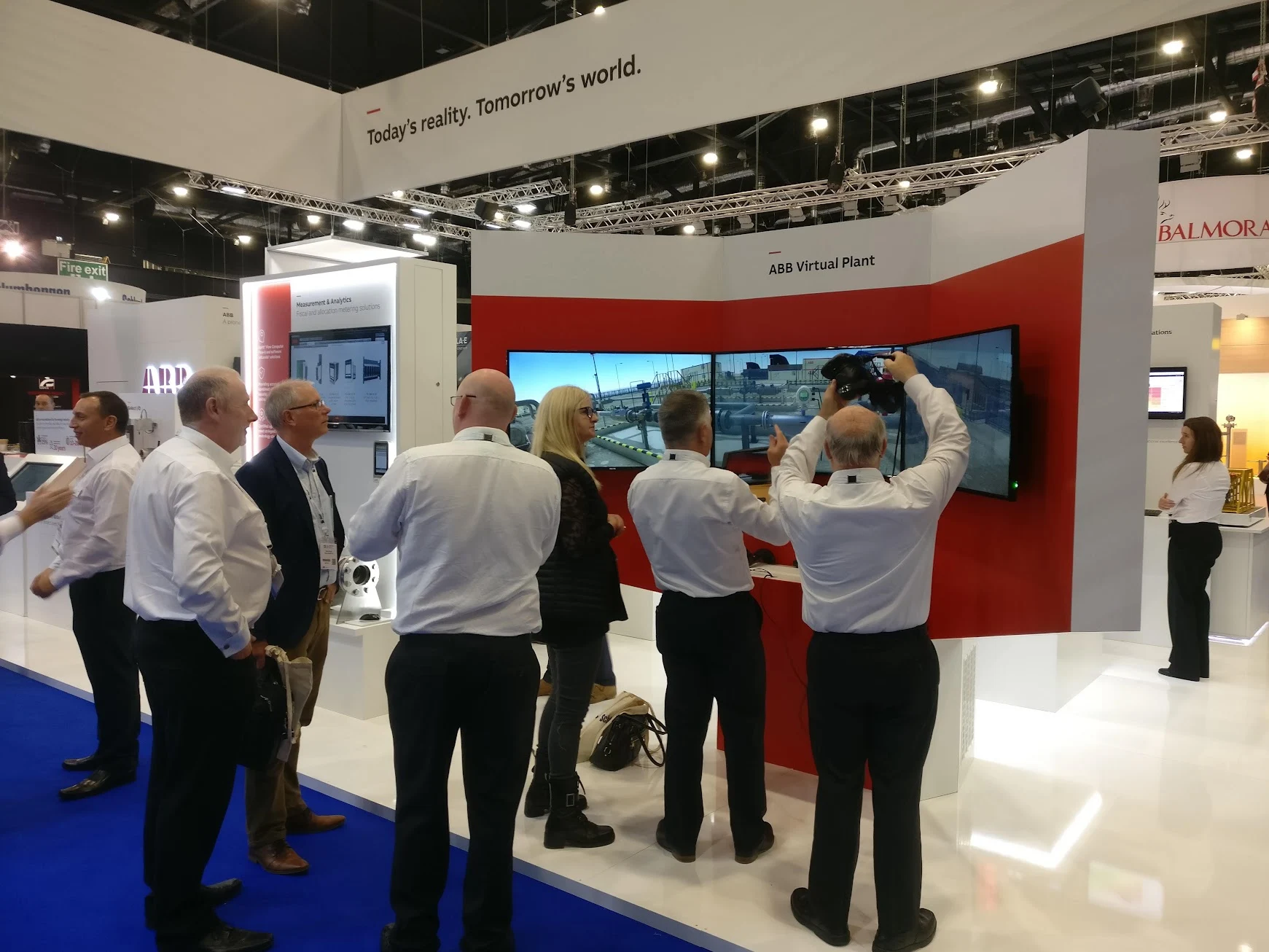 Visitors at the ABB Virtual Plant stand at SPE Offshore Europe 2019, with a triple-screen plant display and a participant lifting a VR headset.