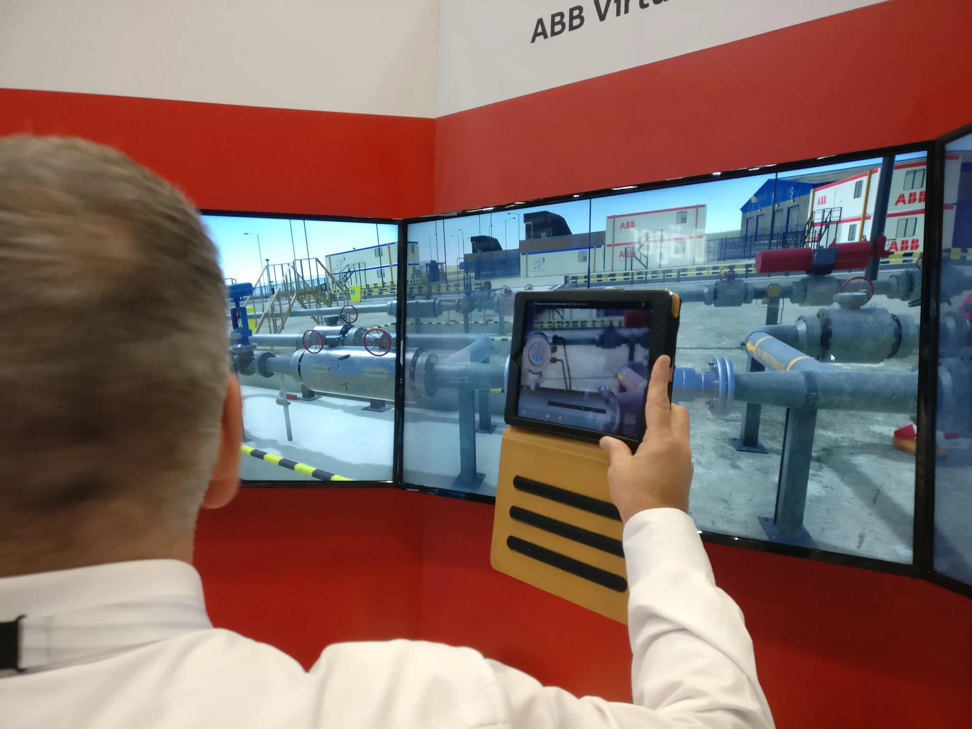 Attendee holding a rugged tablet in front of the virtual wall, with the modelled flow meter visible on the tablet and large screens.