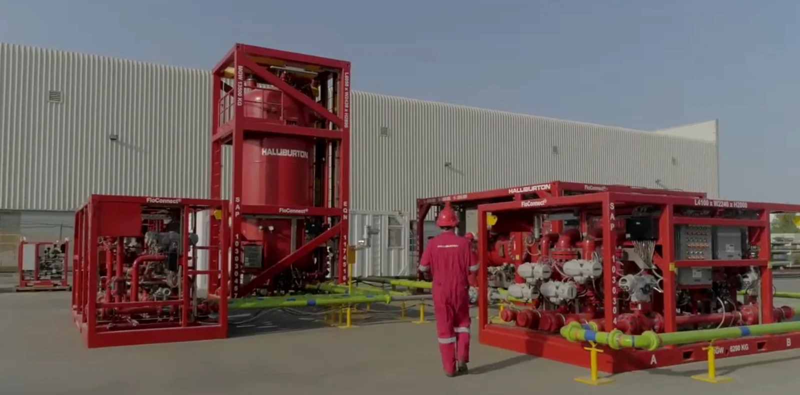 Red Halliburton FloConnect equipment skids connected by pipework outside an industrial building, with an operator alongside.
