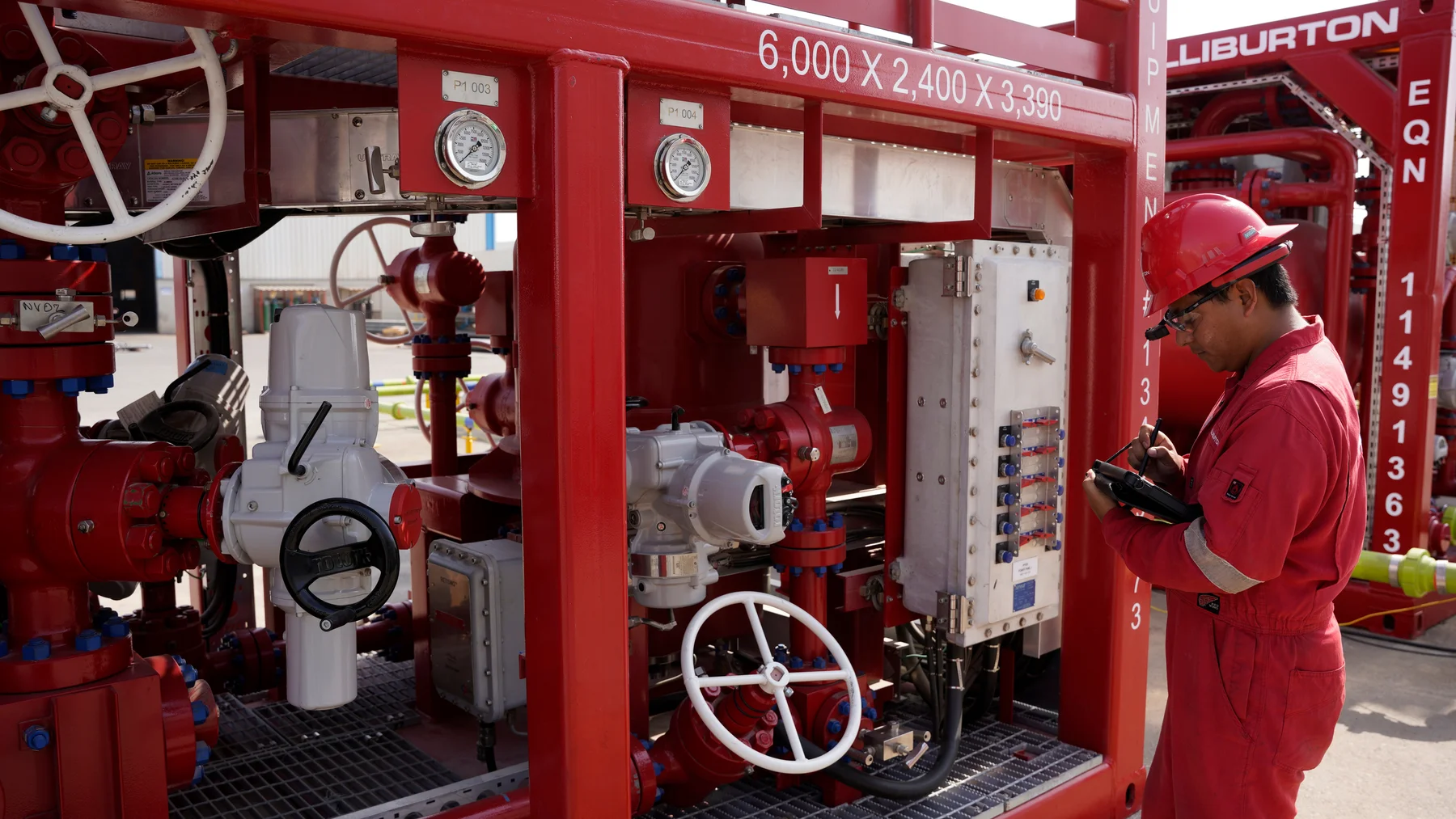 Halliburton operator using a tablet beside well-test valves, actuators and a control panel.