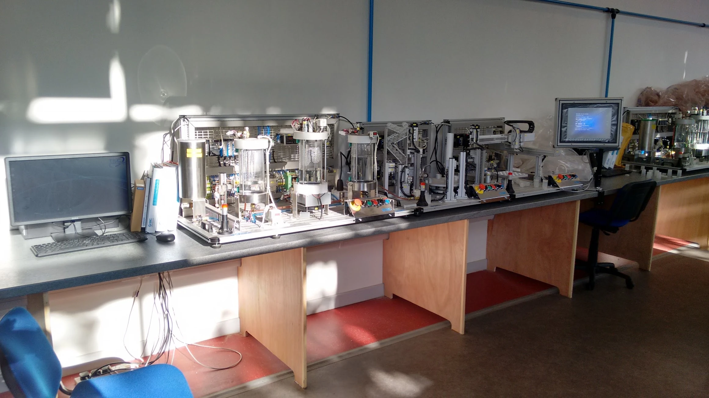 IPC process-control, bottling and handling equipment along the laboratory benches at South Tyneside College, with PC workstations and a mounted Omron HMI.